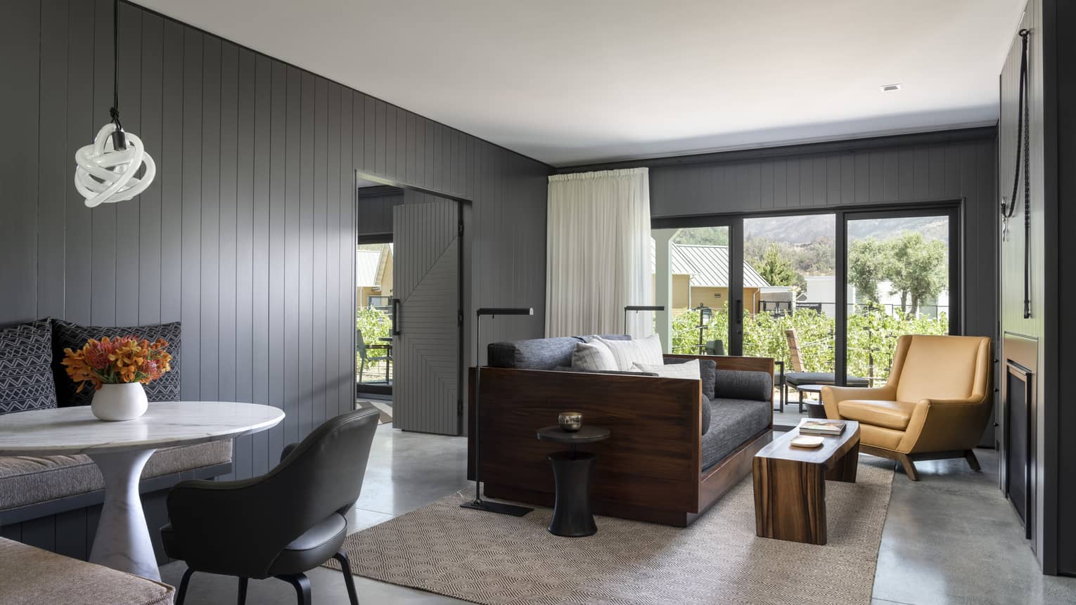 Living room with grey wooden walls, leather chair, sofa, eating area