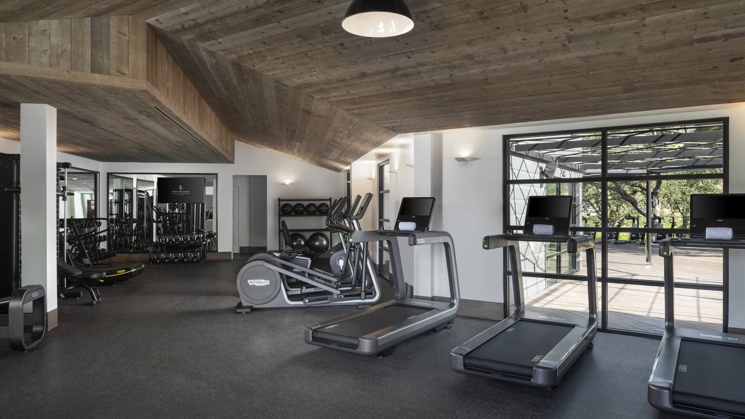 Fitness room with wooden ceiling, three treadmills, windows, ellipticals and weights