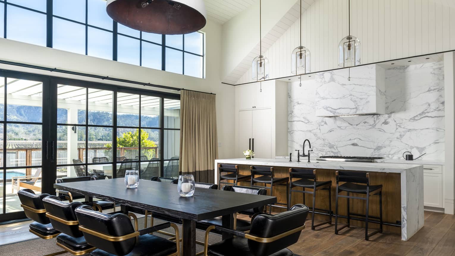 Large vaulted ceiling kitchen with white marble island and wall, a dining table with 8 leather chairs