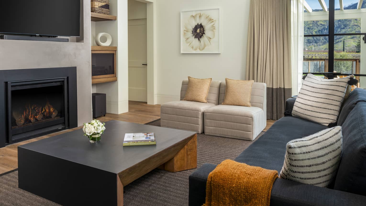 Living room with dark grey sofa, two light grey chairs, large black coffee table, fireplace and TV