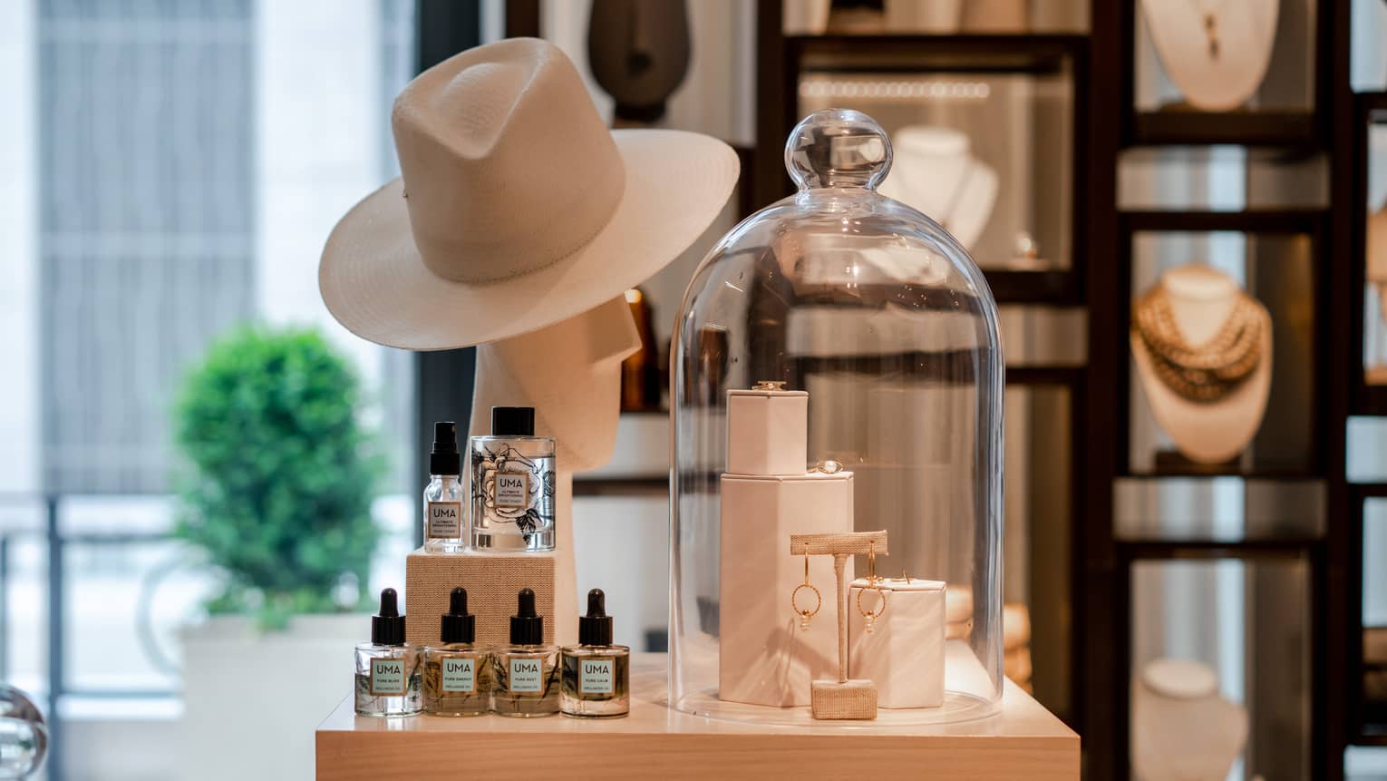 A boutique display of gold jewelry, a beige wide-brimmed hat, and wellness skin care products