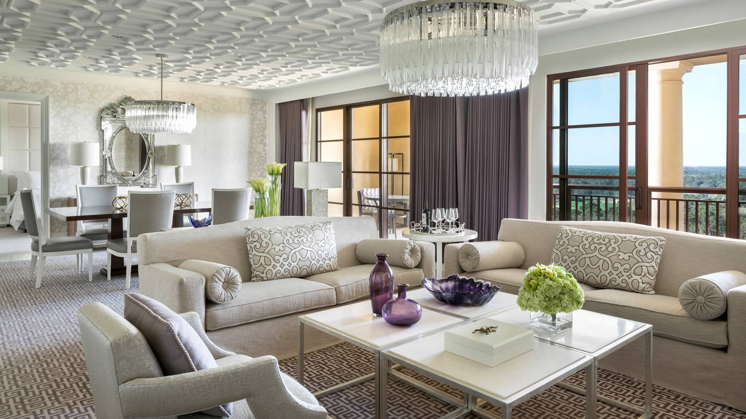 Grand Suite white sofas, armchair around coffee table with purple vases under crystal chandelier, sunny windows