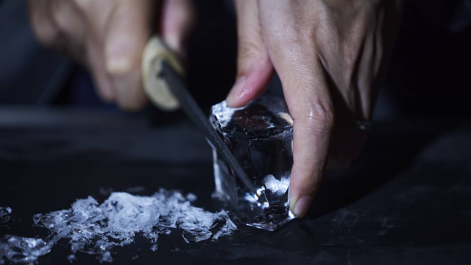 Hands shave ice off a larger housemade ice cube at luxury bar