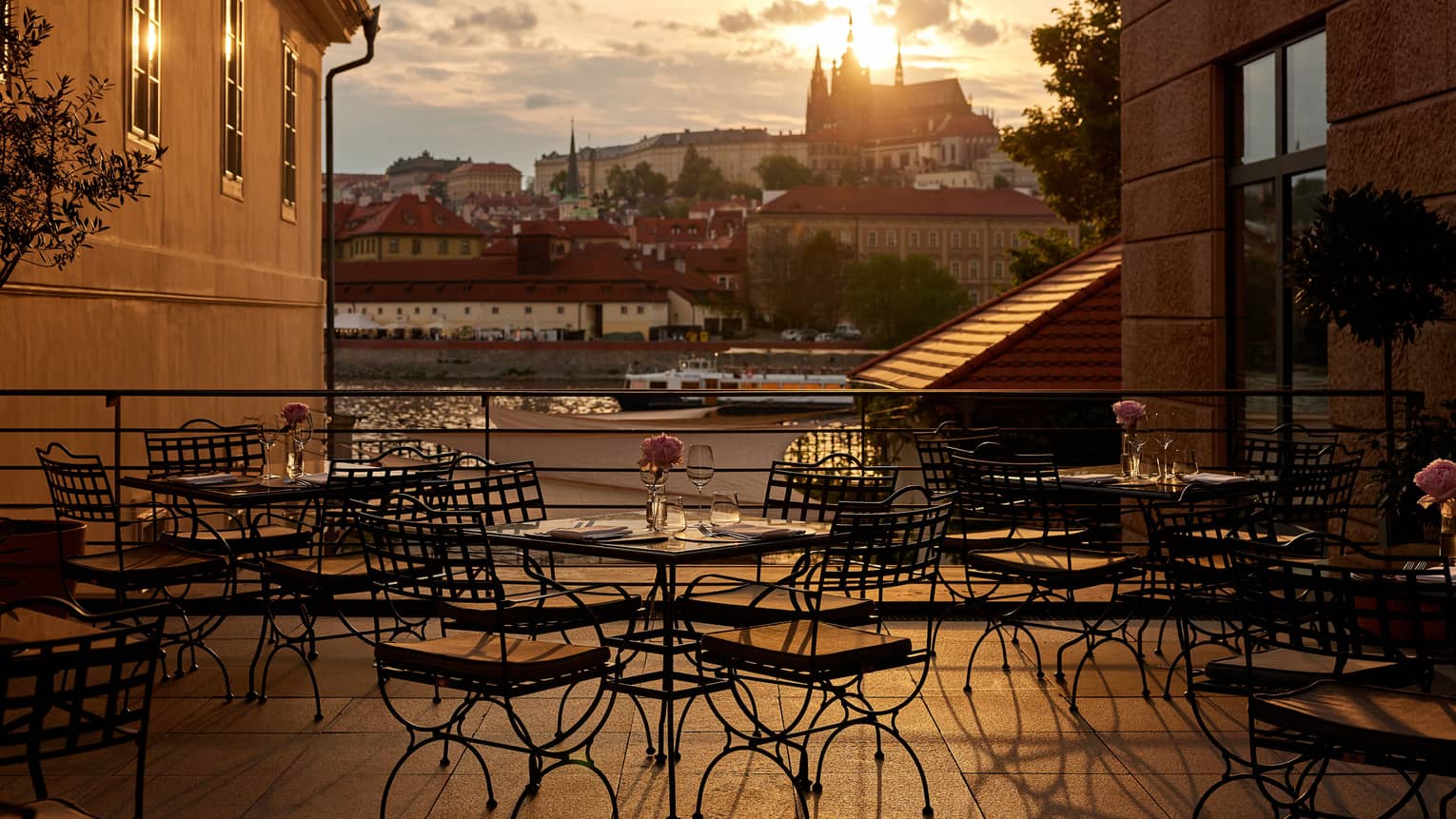 Restaurant terrace with black bistro dining tables with views of the Vltava River and Prague Castle at sunset