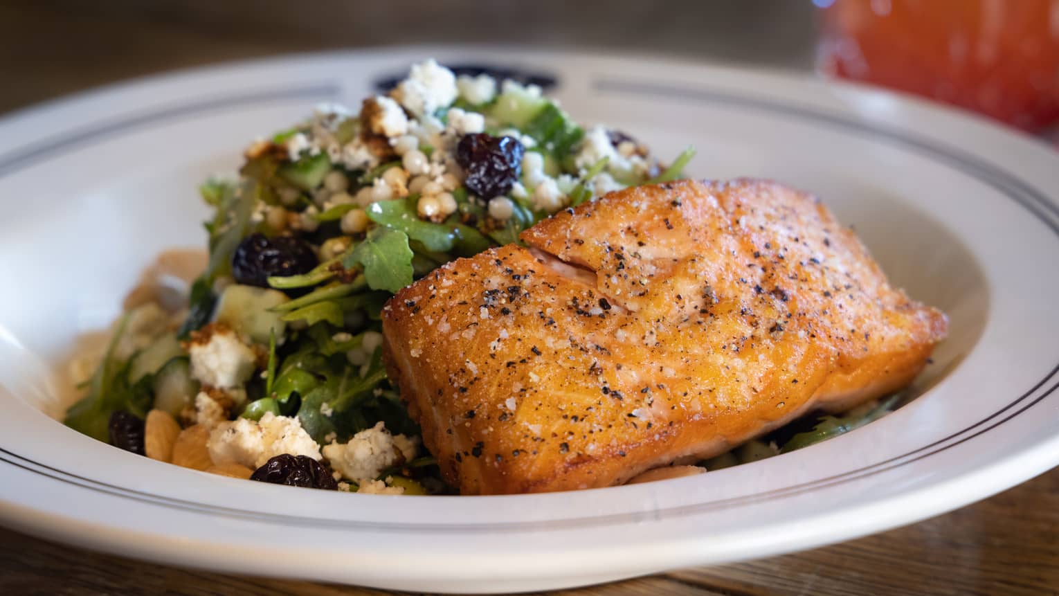Salmon with a green salad in a white bowl.