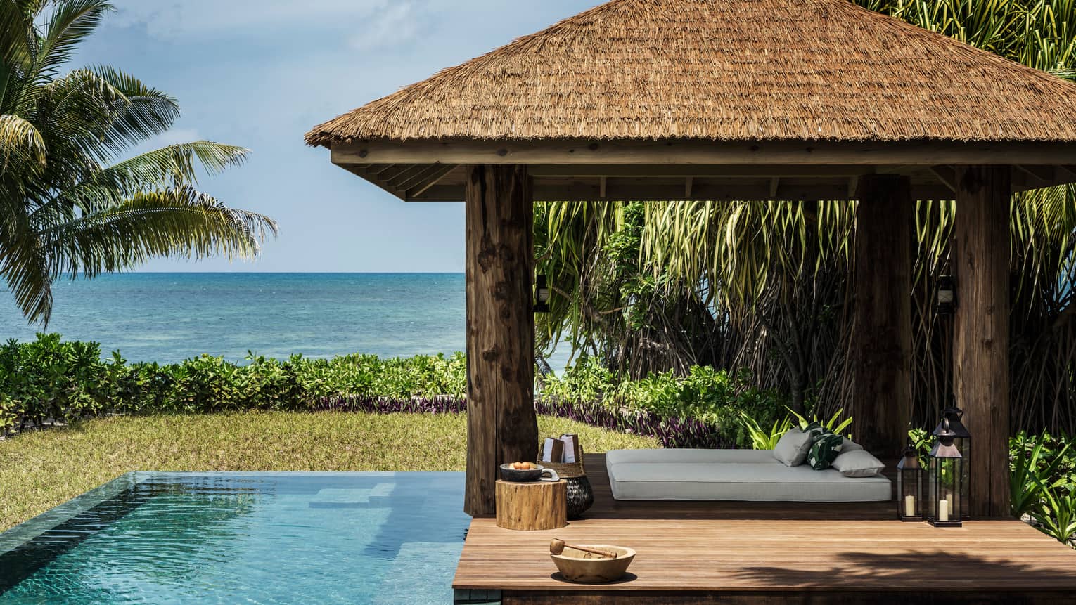 Four-pillar wooden cabana and infinity edge pool, sea in the distance