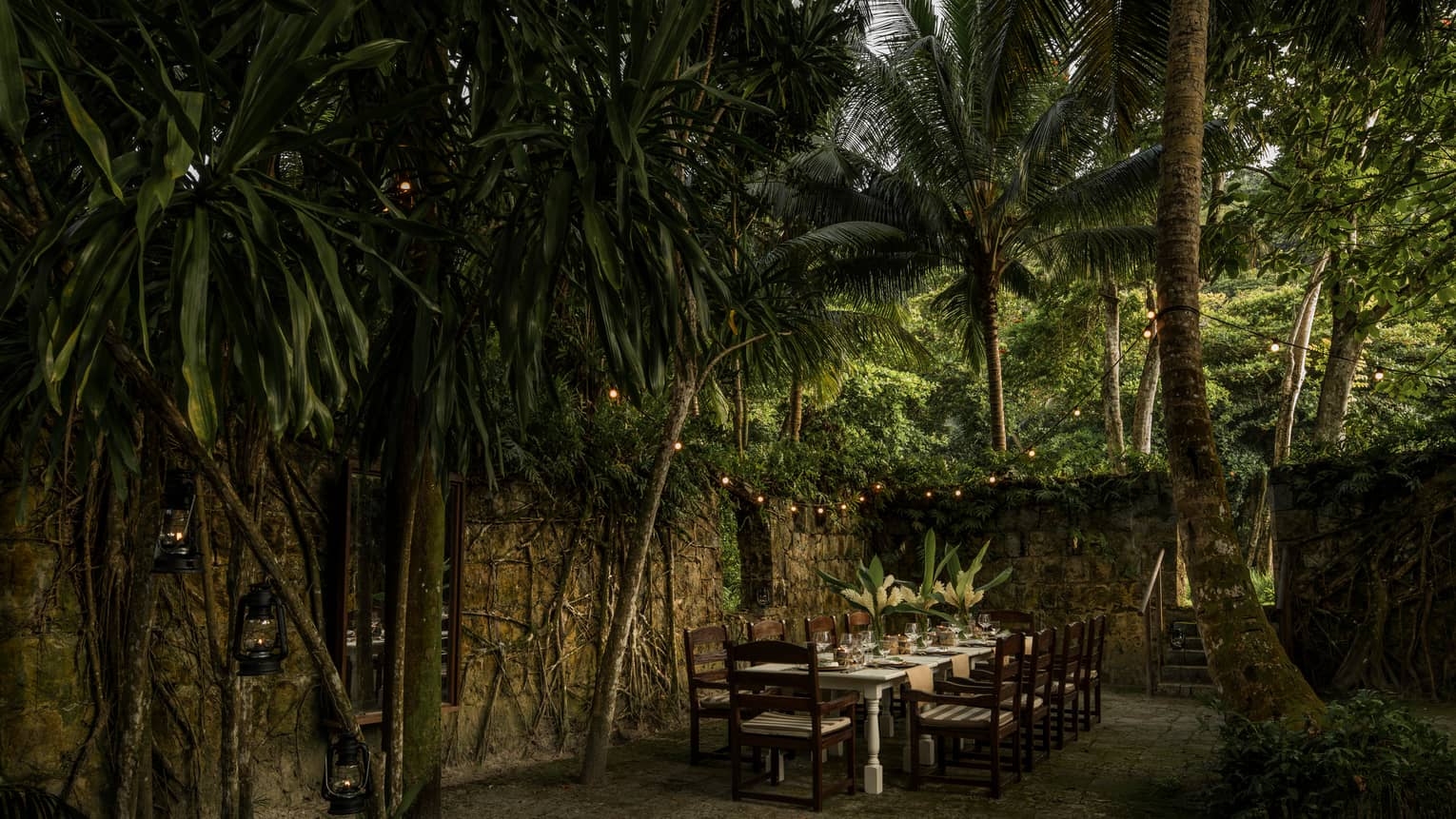 Long dining table with chairs outdoor under palm leaves, near the Foumba Creole ruins at Kannel restaurant