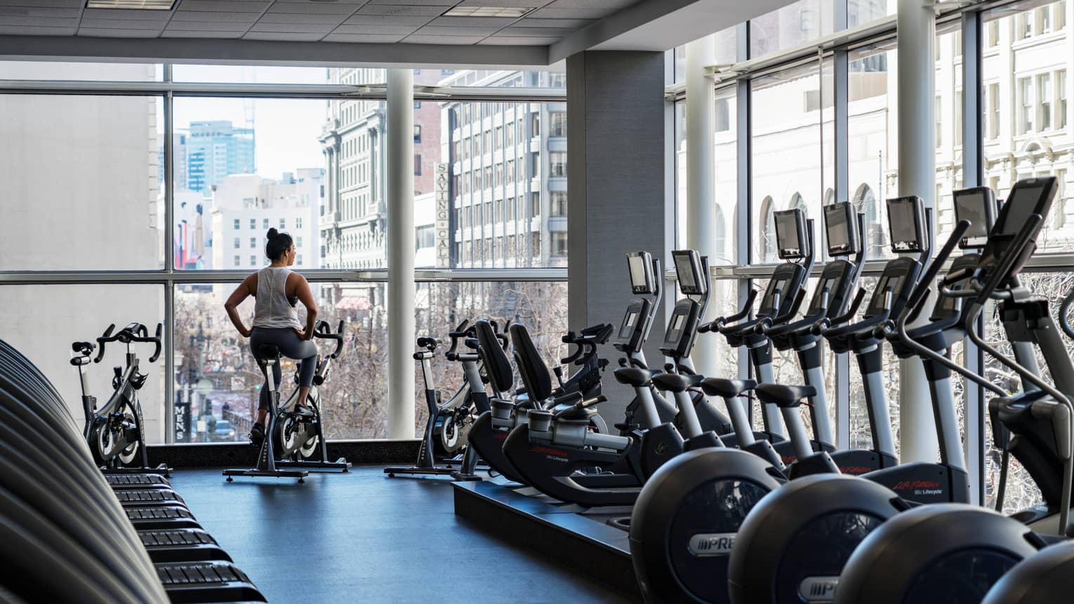 Equinox Fitness Centre, woman on exercise bike by floor-to-ceiling windows, row of cardio machines