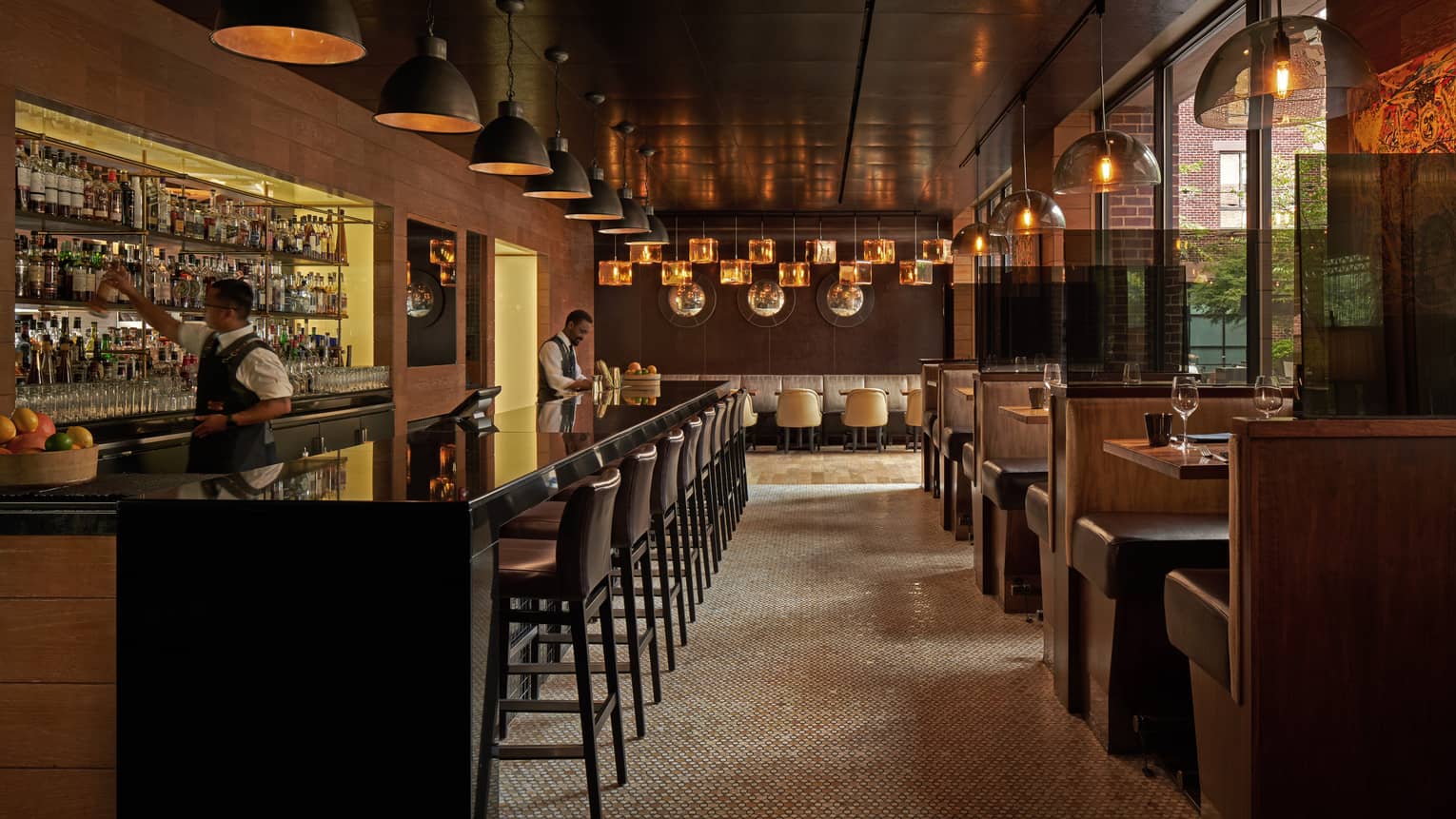 A dimly lit bar with dark wood stools and booths.