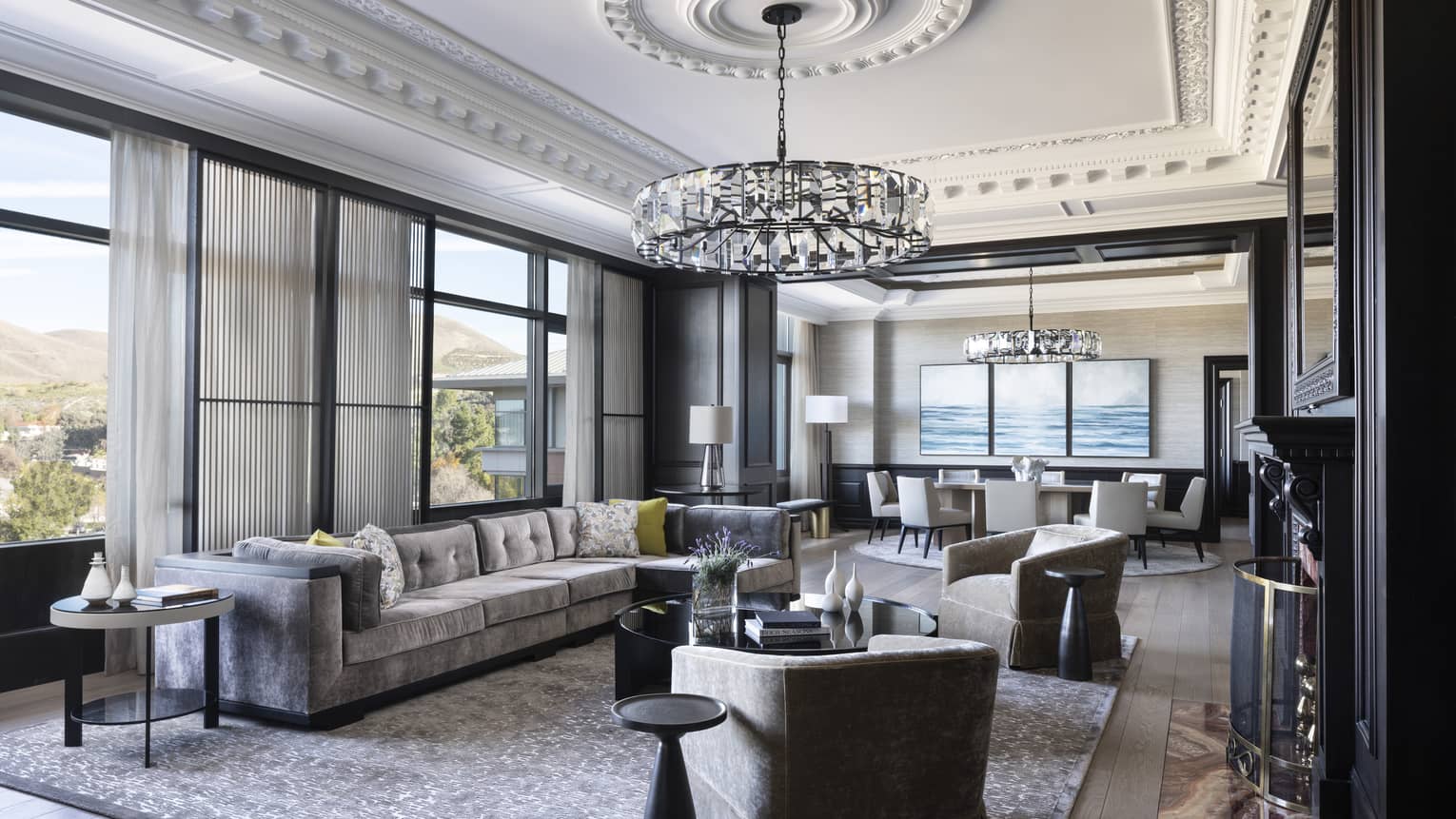 Presidential Suite featuring a chic, grey, L-shaped sofa under a ceiling that boasts elaborate crown molding and a crystal chandelier