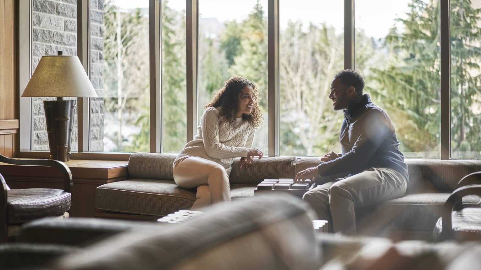 Couple lounge on sofa by floor to ceiling windows overlooking forest