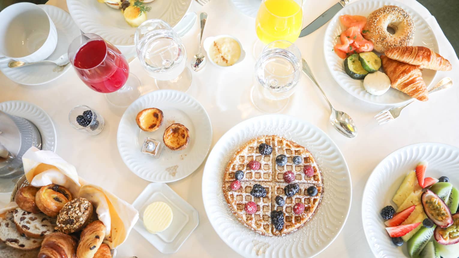 Aerial view of breakfast table with waffles, fresh fruit, pastries and juice in wine glasses