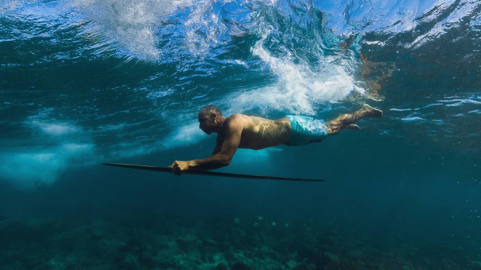 Surfboard designer Bonga Perkins dives under the water on a wooden surfboard
