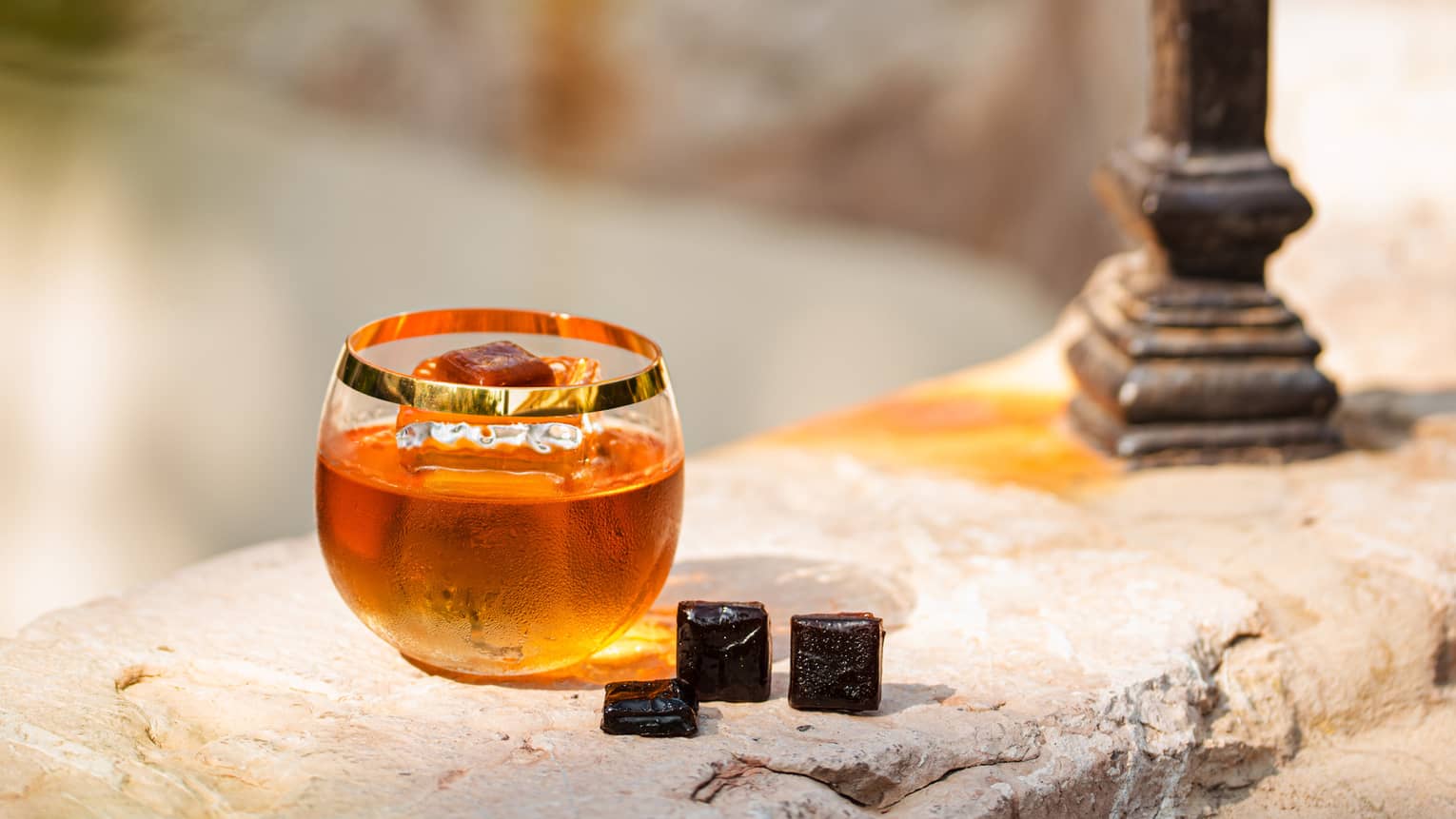 A glass of amber coloured alcohol on a stone wall.