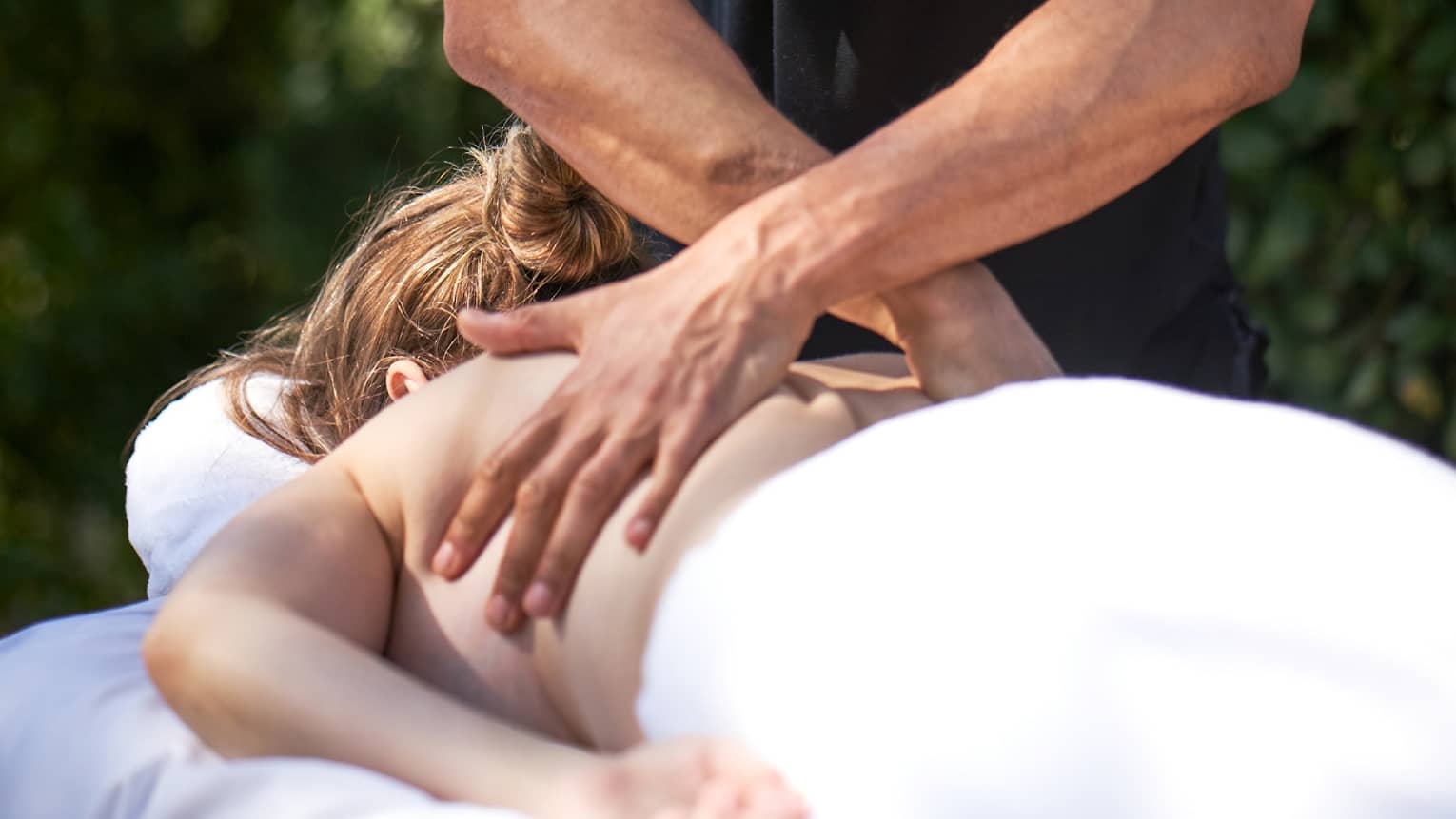 Man crosses hands over woman's back as she lays on outdoor massage table