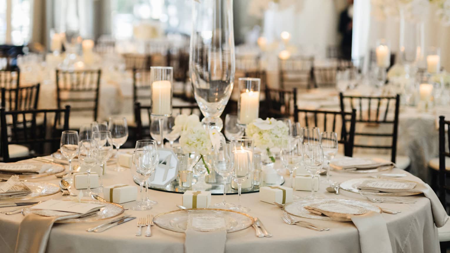 Round wedding banquet table with glassware, candles under tall white floral arrangement