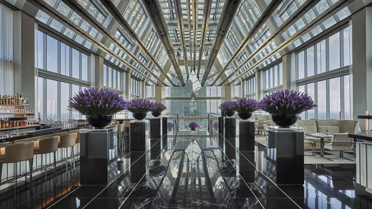 Bar beside purple flowers in black planters, marble floor under glass loft penthouse ceiling