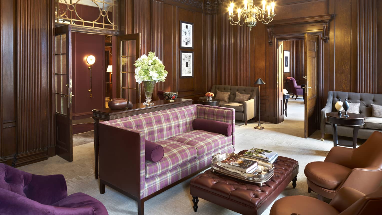 Purple plaid loveseat, velvet and leather armchairs, bench in room with dark wood panel walls