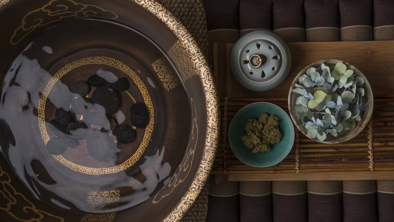 Looking down at spa bowl with water, black stones, small round dishes with flowers