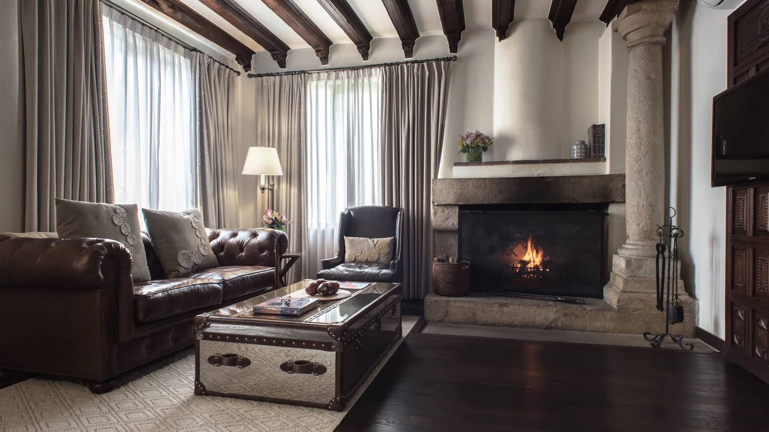 Living room with wooden beams on ceiling, dark wood floors, leather sofa, fireplace