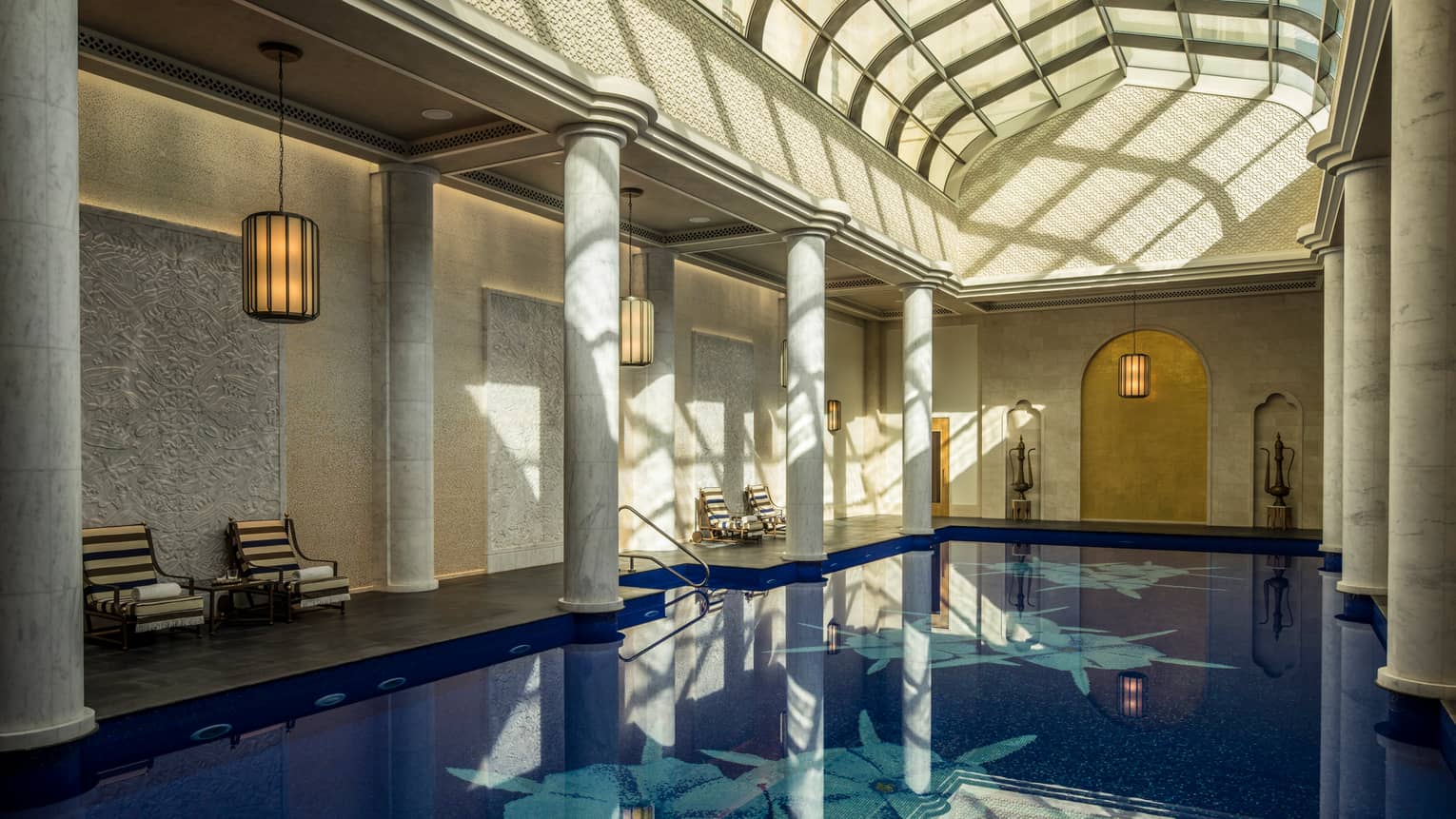 Long indoor swimming pool under curved skylights and tall white pillar columns