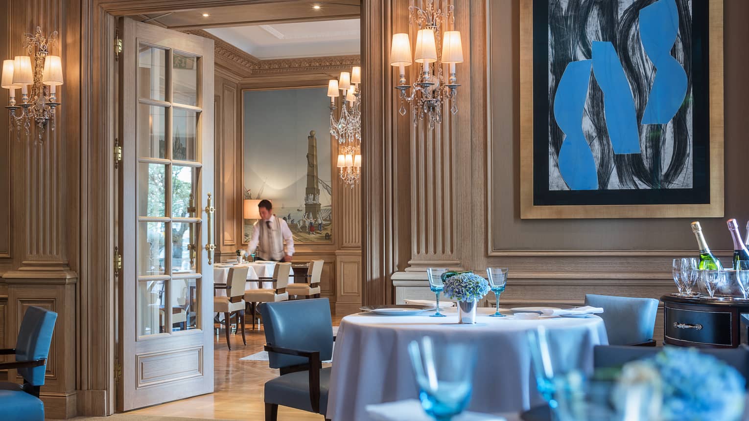 Il Lago dining room with high ceilings, cream walls and bright blue painting, chairs, glassware
