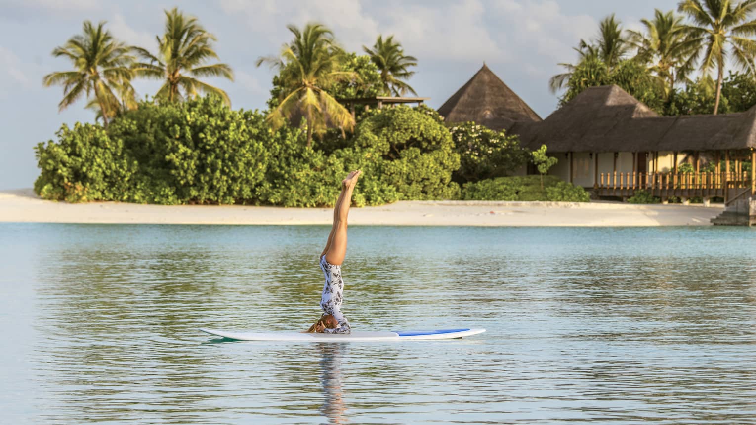 Woman balances on arms during stand-up paddleboard yoga session on Indian Ocean