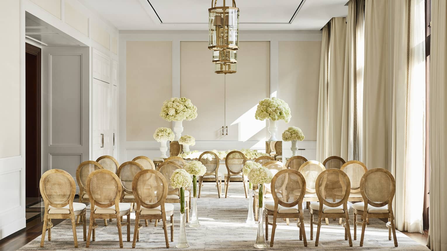 Event room with gold hanging lights, three rows of upholstered chairs set up for event
