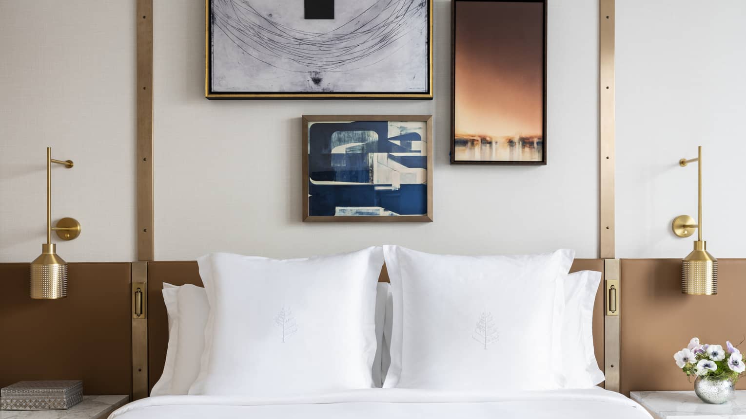 Bed with white sheets and shams, three framed artwork on wall overhead