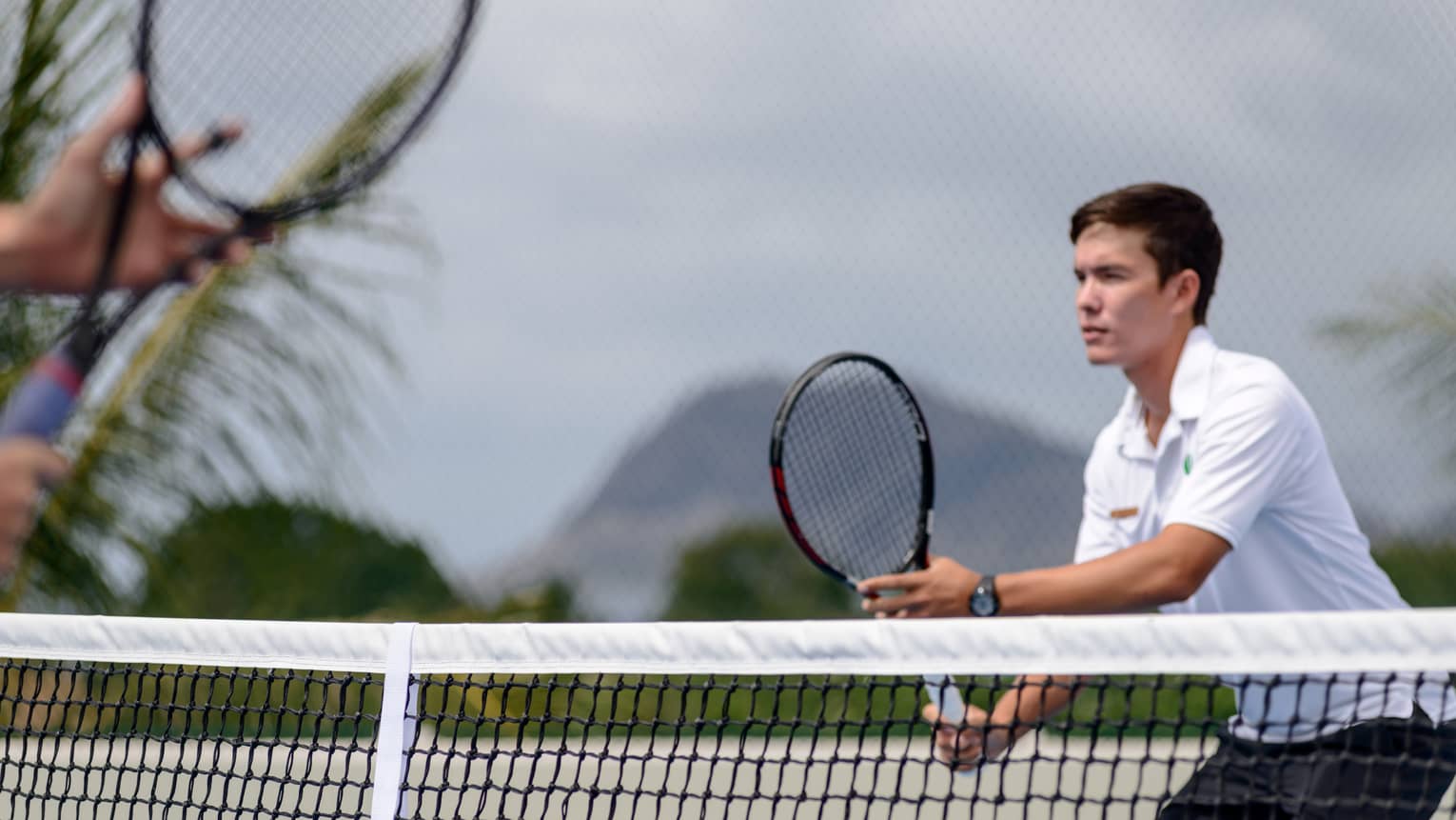 Man holds tennis racket near net in the Four Seasons Oahu Resort tennis centre