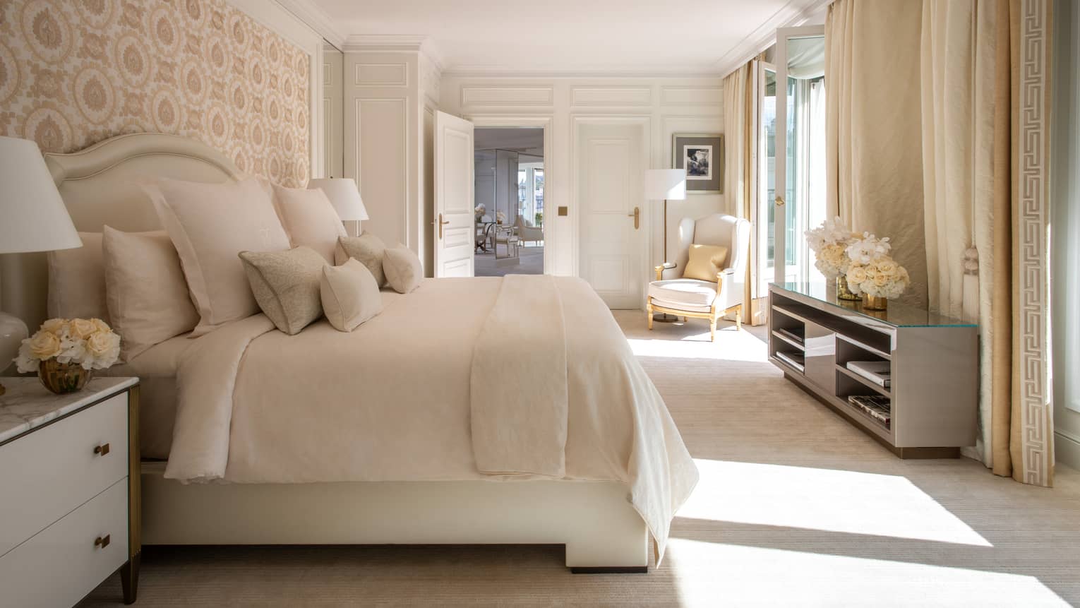 Bedroom with pattern wallpaper, cream bedding and carpet, dresser, windows