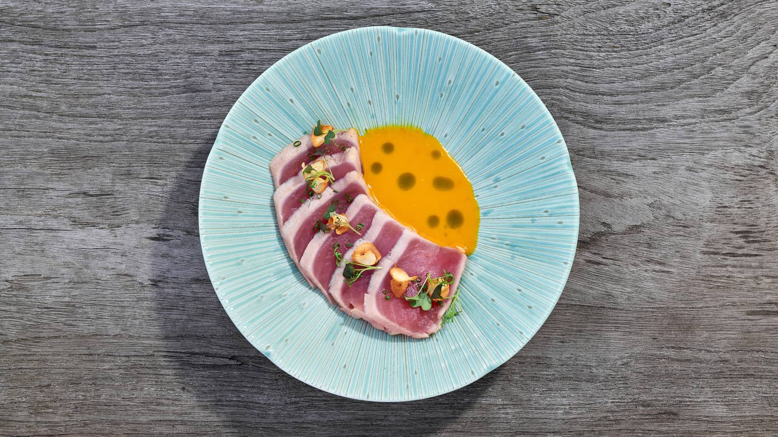 Sliced seared tuna fanned beside Amarillo sauce on light blue dish