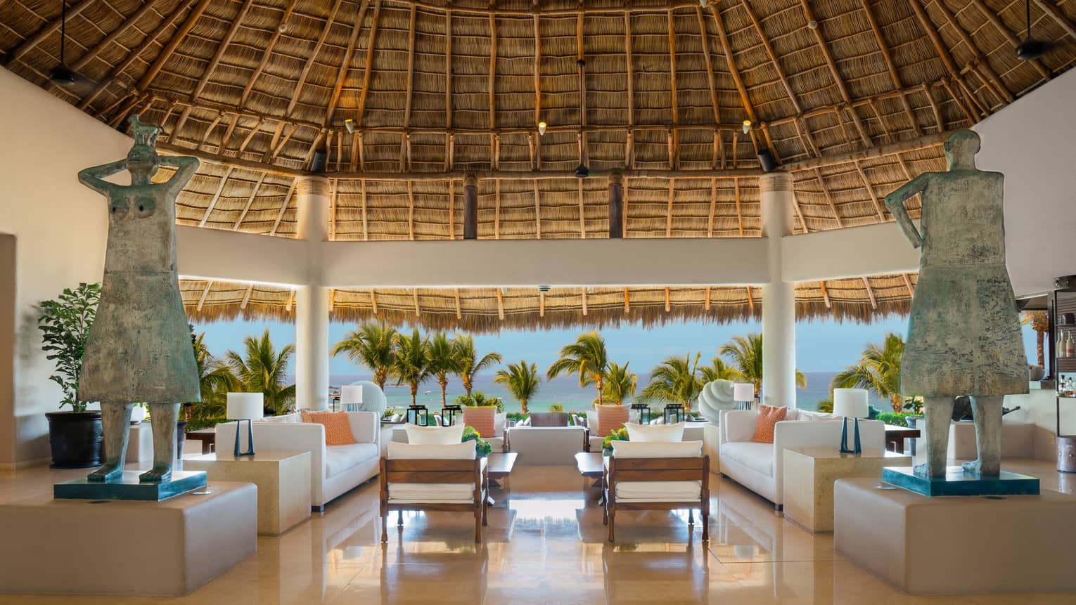 Indoor-outdoor lobby area with two sofas and two arm chairs under thatched-roof ceiling