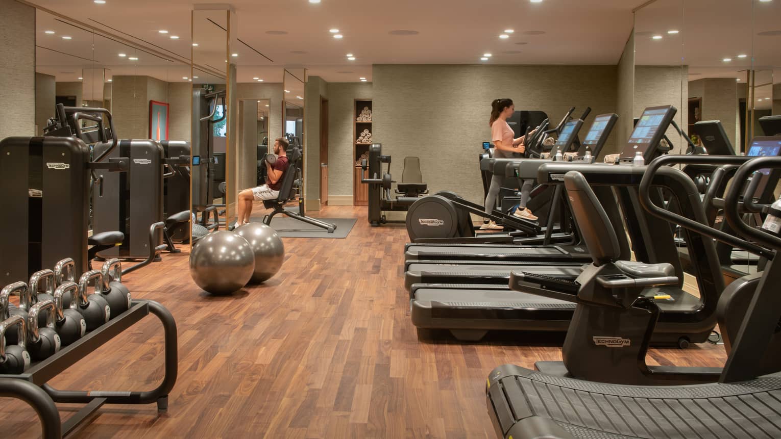 Indoor gym with a woman on the elliptical, three treadmills, free weights