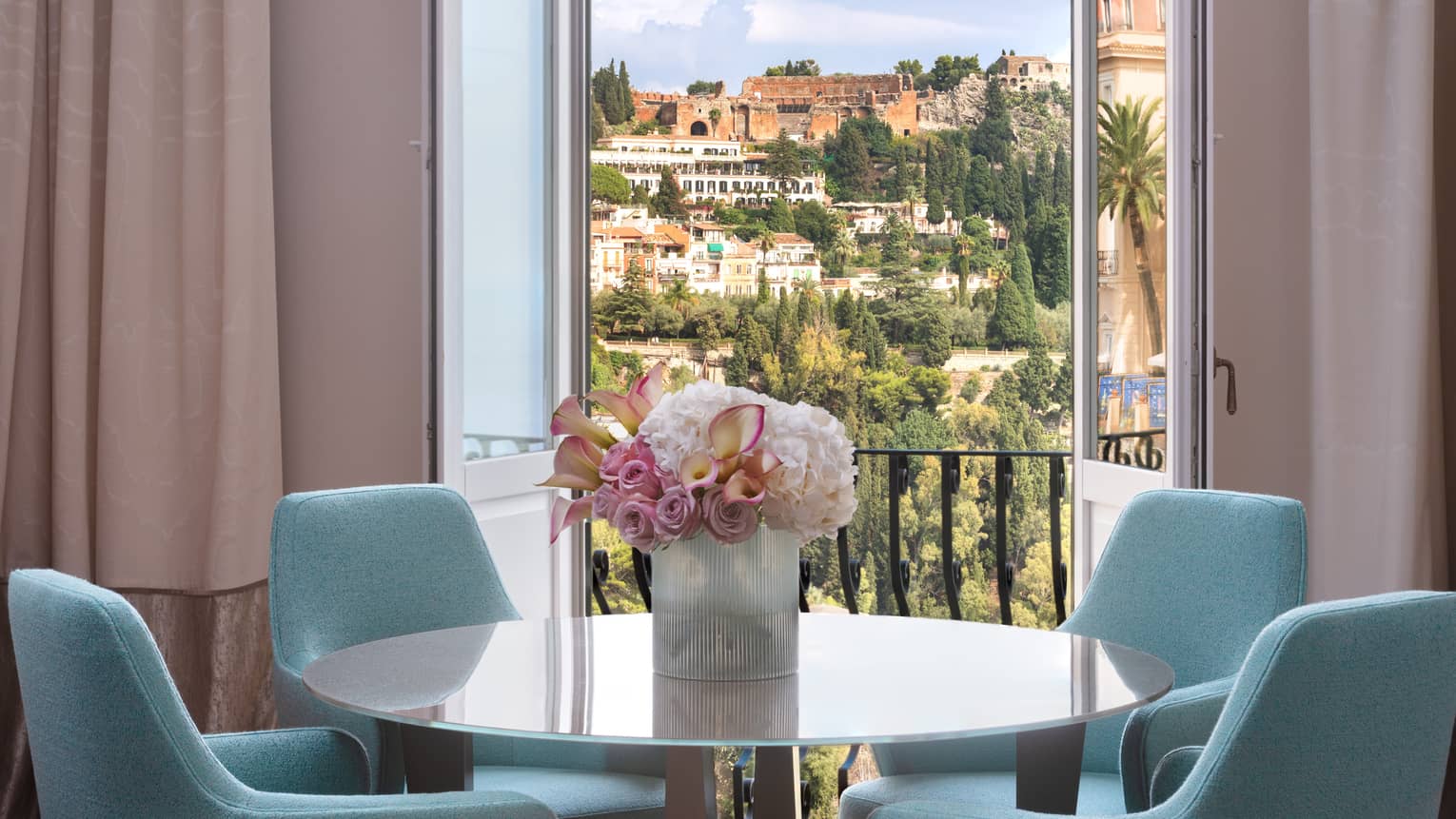 Round dining table, pink flowers, four turquoise chairs, doors opening to balcony