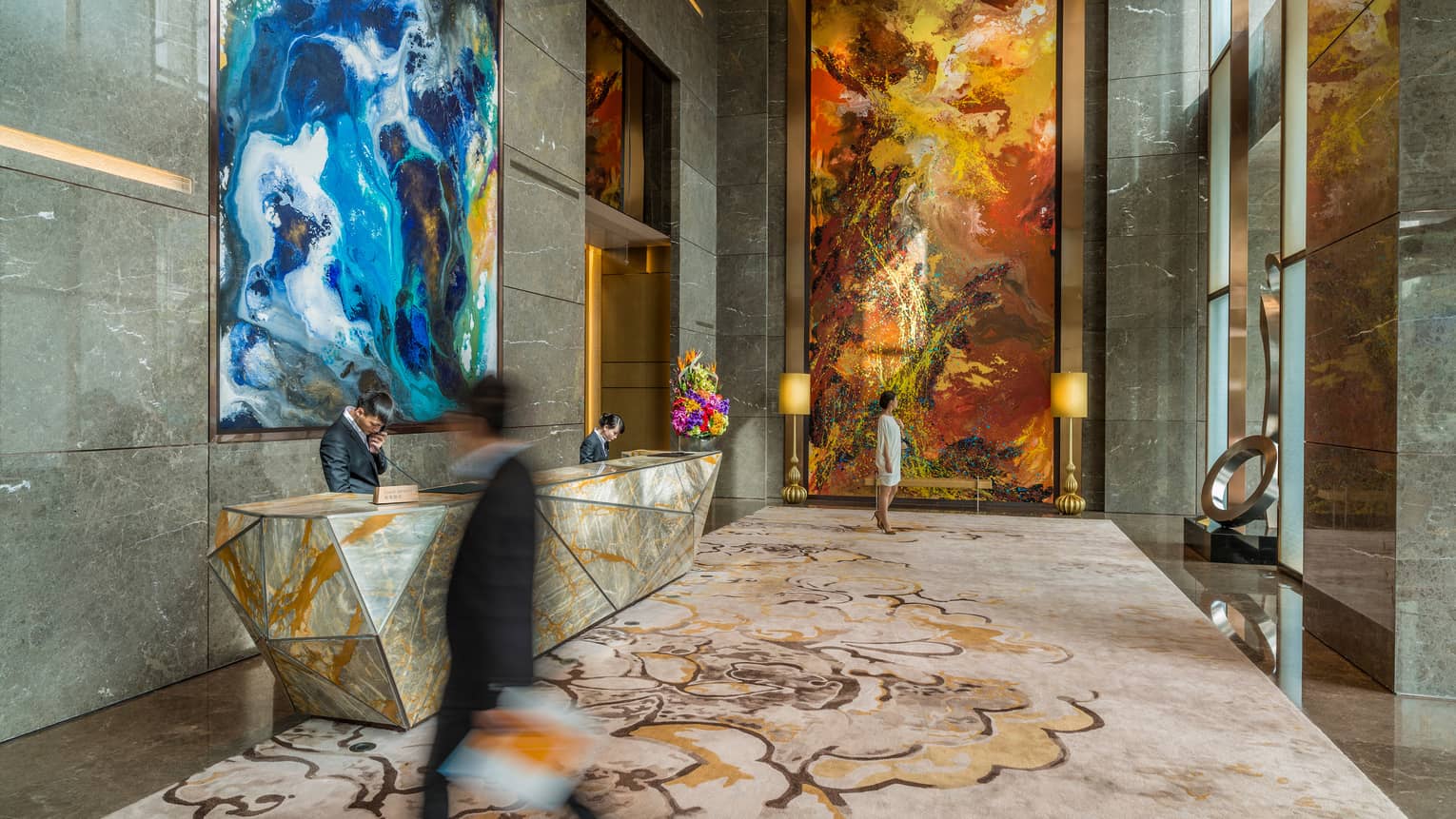 Man wearing suits walks through hotel lobby surrounded by marble, large modern art 