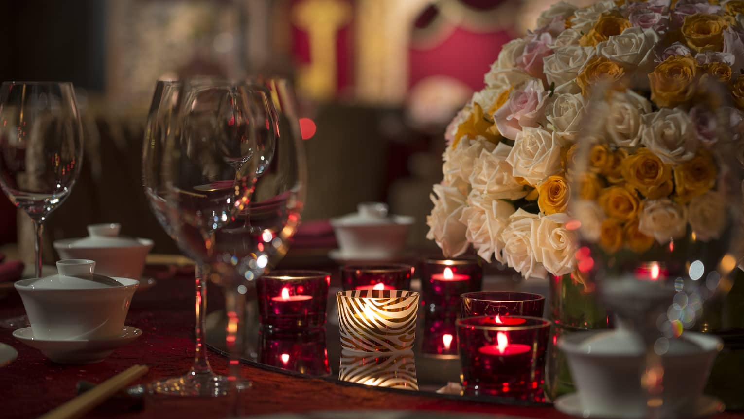Close-up of red candles, pink and white roses and wine glasses on banquet dining table
