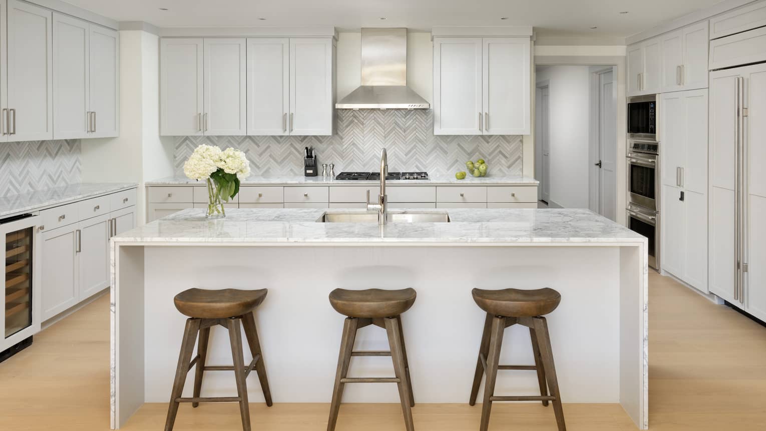 three natural wooden stools are set up next to a white marble topped island in a very neutral kitchen