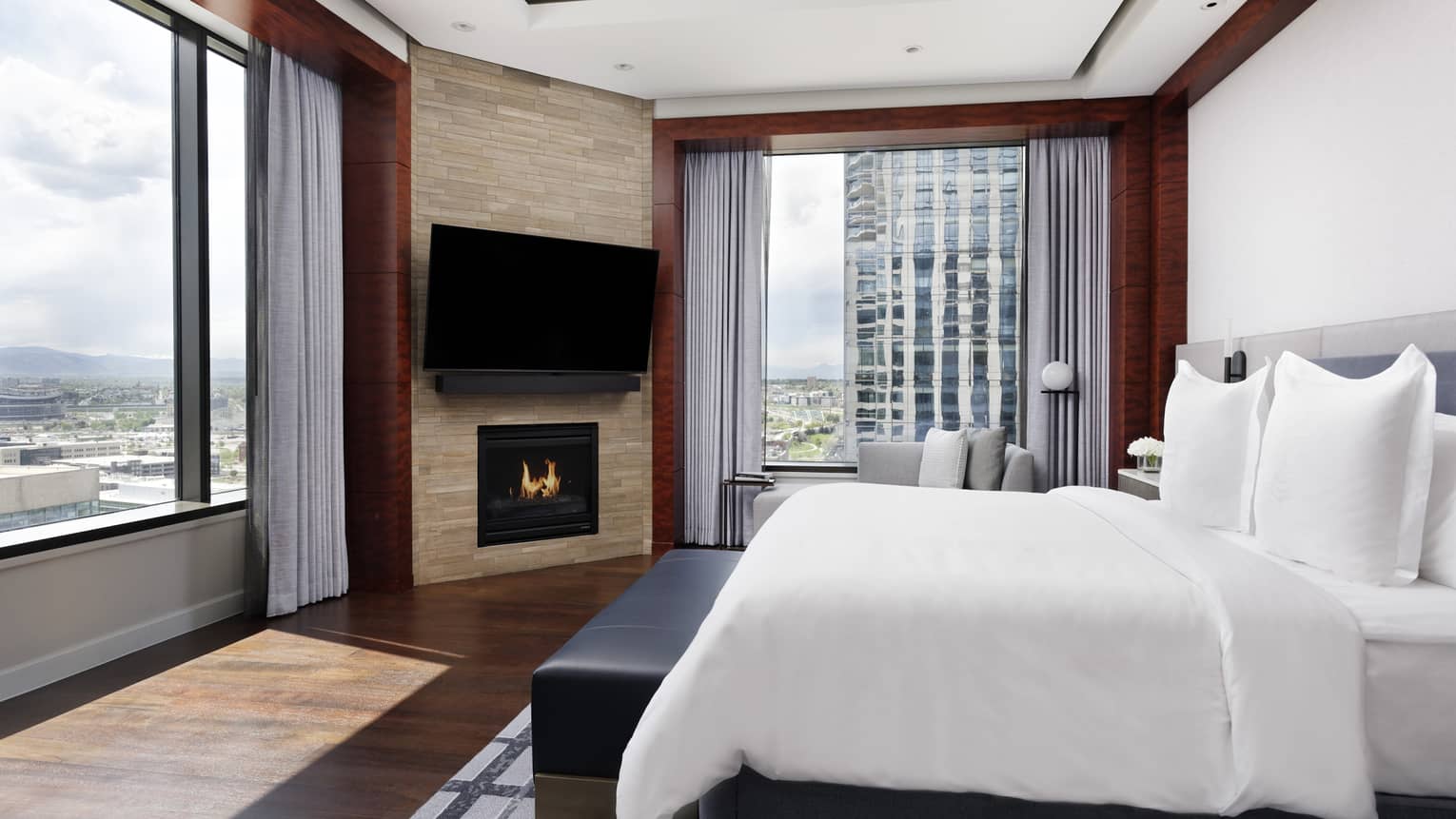 Corner guest room at Four Seasons Hotel Denver. City views through two large windows, king bed, fireplace, wall-mounted TV.