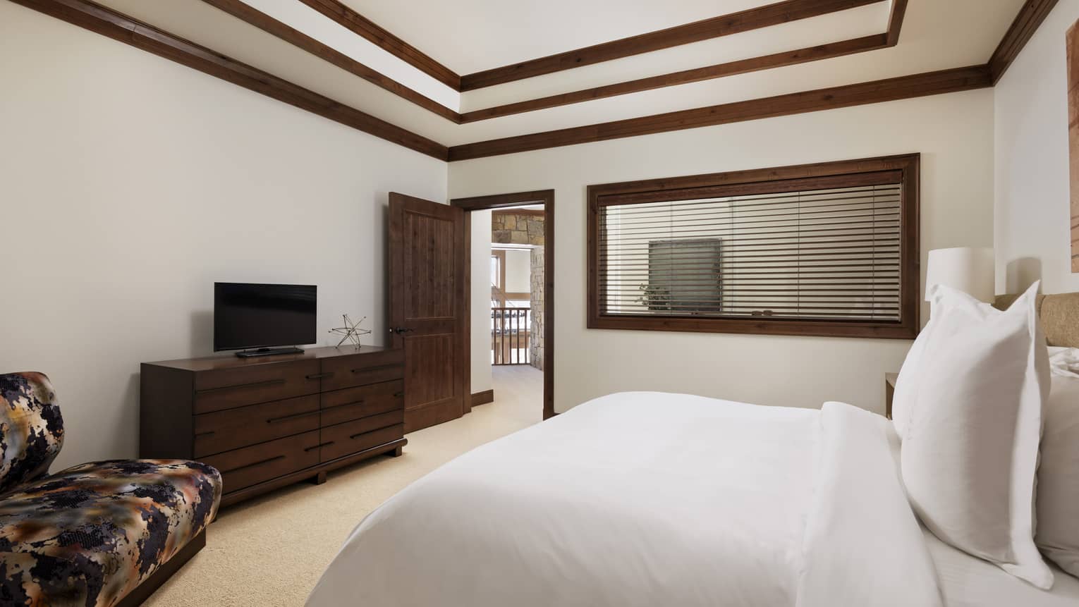 Bedroom with single bed, wooden dresser and TV, vaulted ceiling with dark wood crown molding