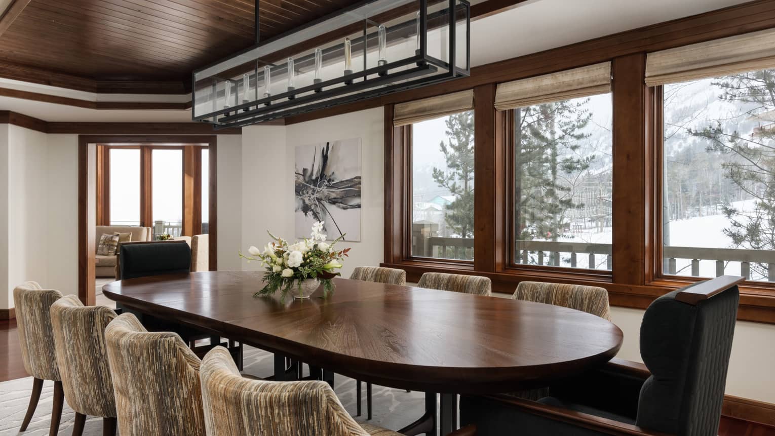 Living room with large wooden table, 10 upholstered chairs, ski slope view