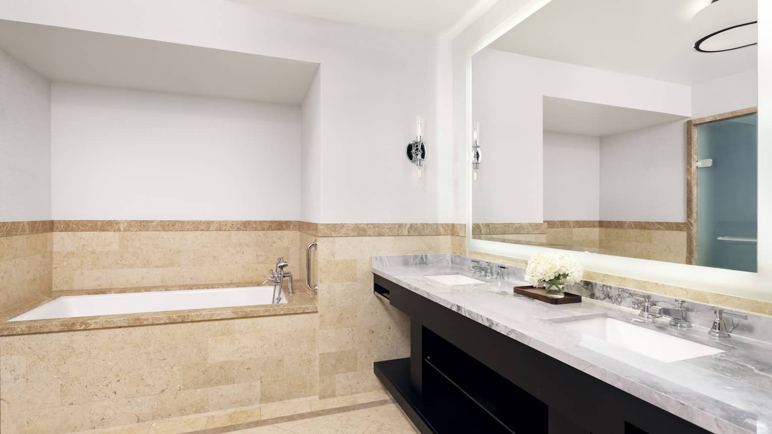 Bathroom with built-in tub, limestone walls and floor, marble double vanity and black wooden cabinets