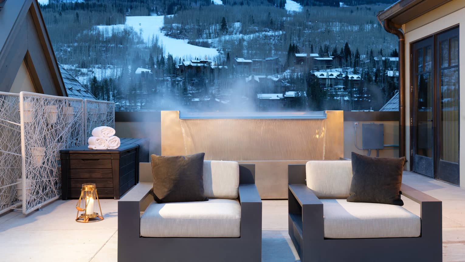Plush patio armchairs in front of steaming fountain, snowy mountains in background