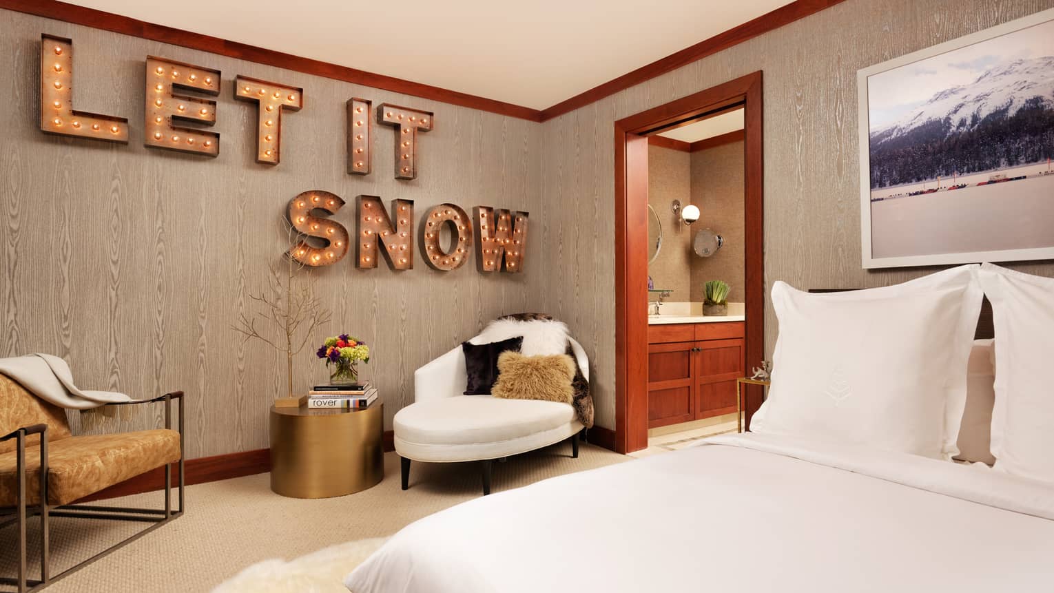 Bed across from two armchairs, brass table, large sign with lights reading Let It Snow on wall