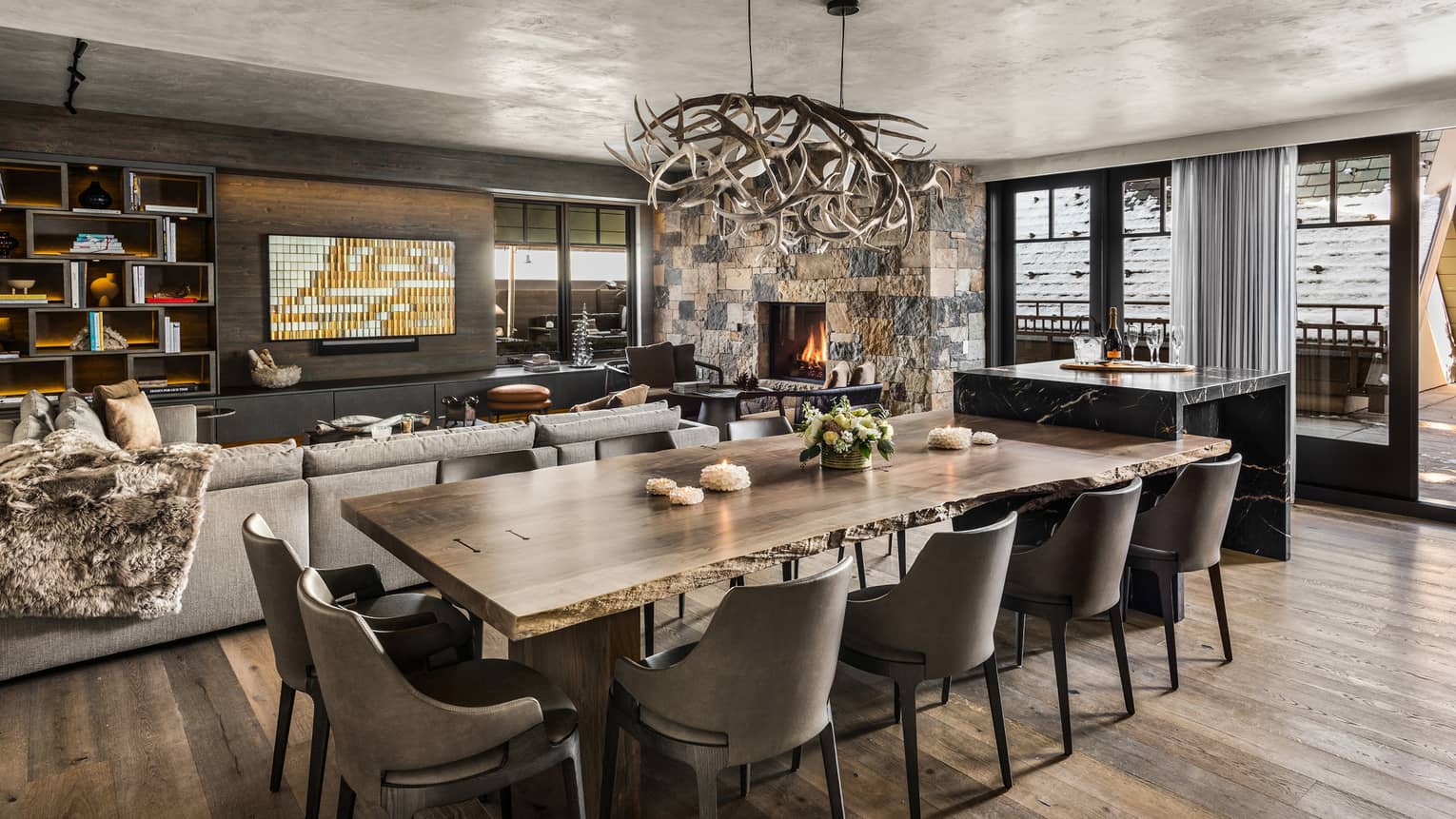 Mountain-chic dining area with wooden floors, dining table and ten leather chairs, antler chandelier