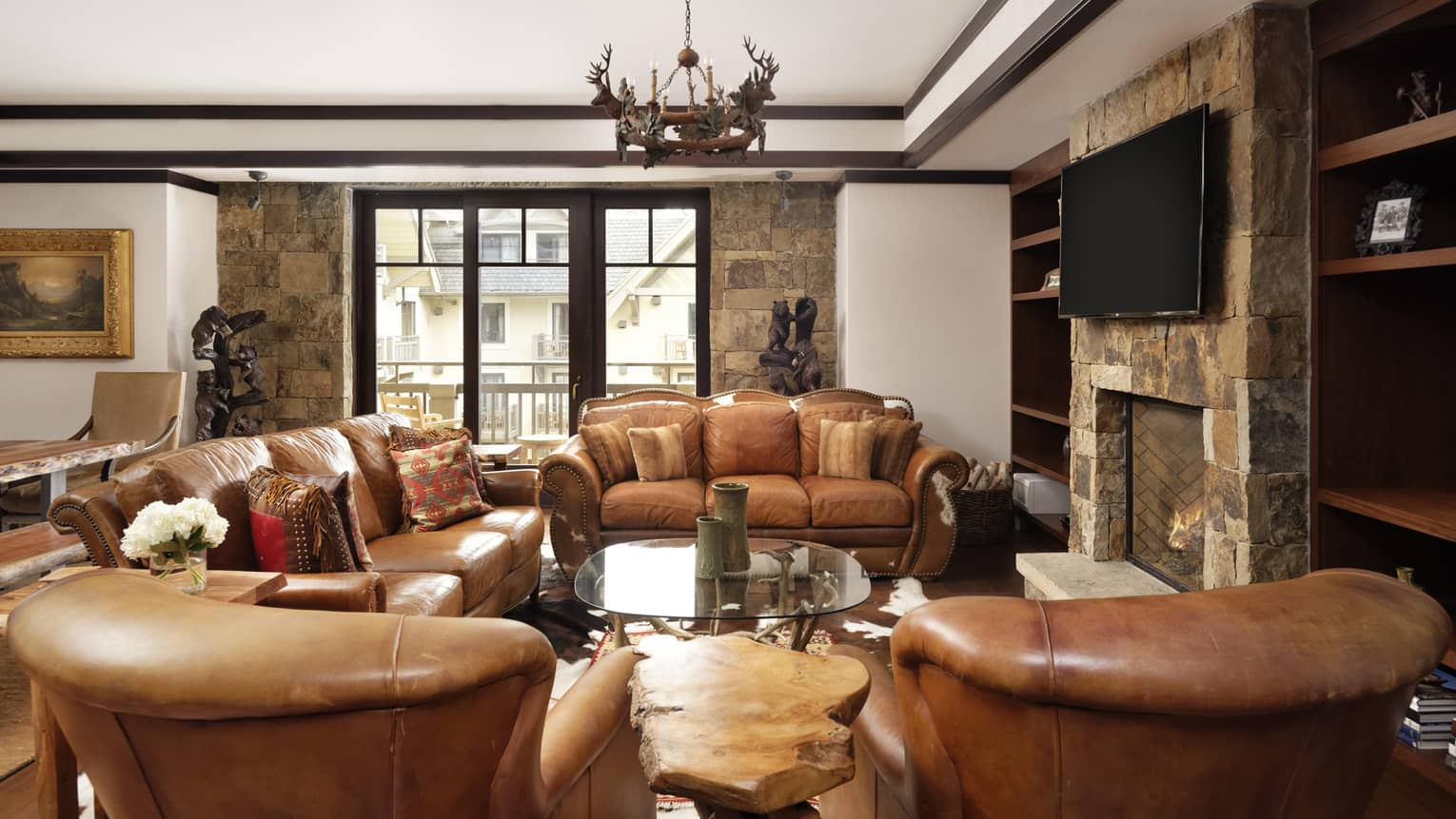 Mountain-chic living room with two brown leather sofas, two matching arm chairs, antler chandelier