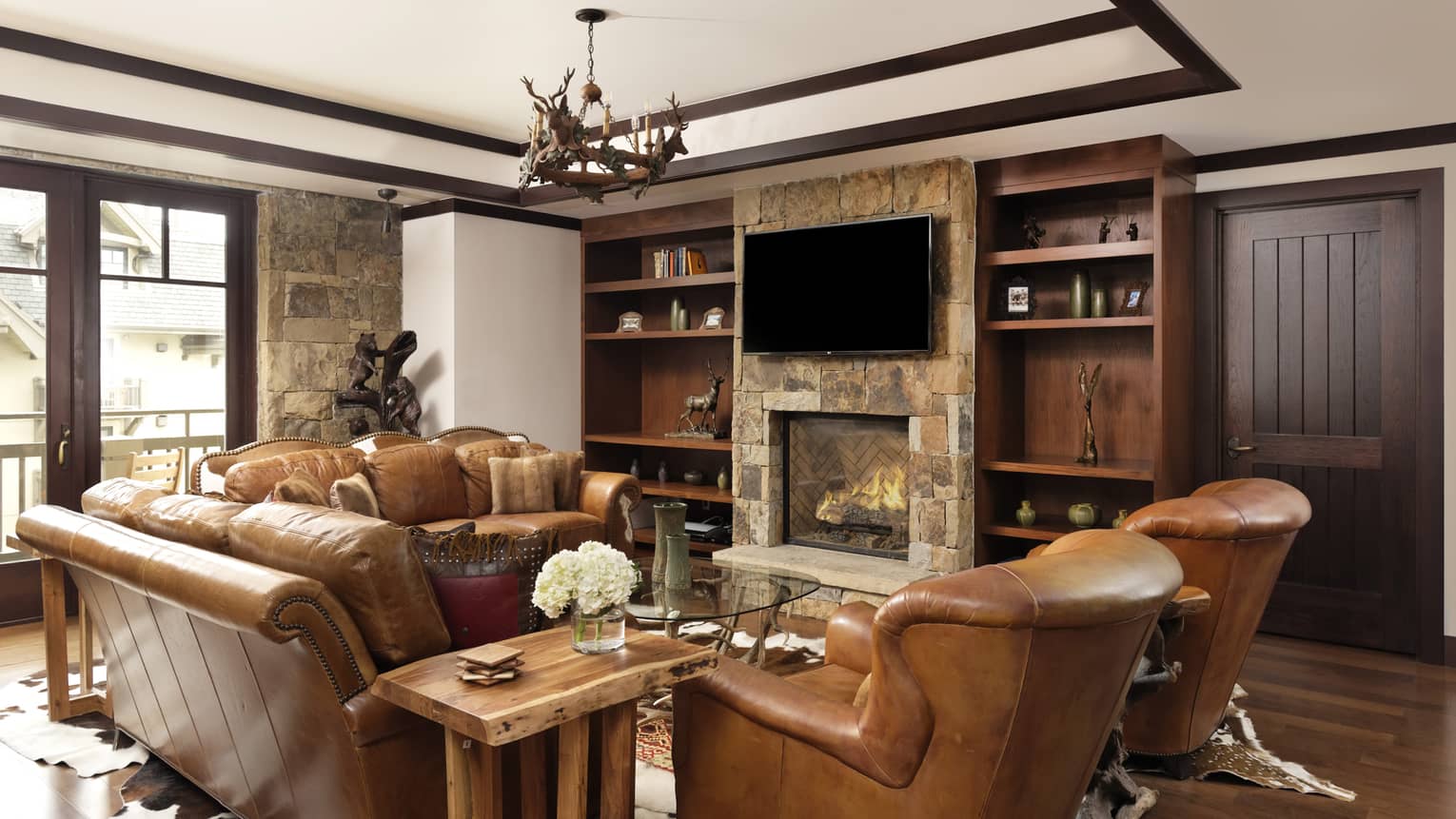 Mountain-chic living room with two brown leather sofas, two matching arm chairs, stonework fireplace