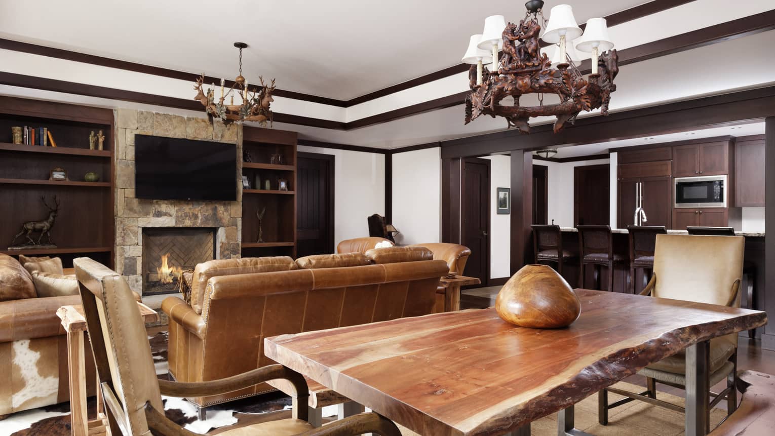 Large dining table made of rustic wood, next to living room with brown leather sofas
