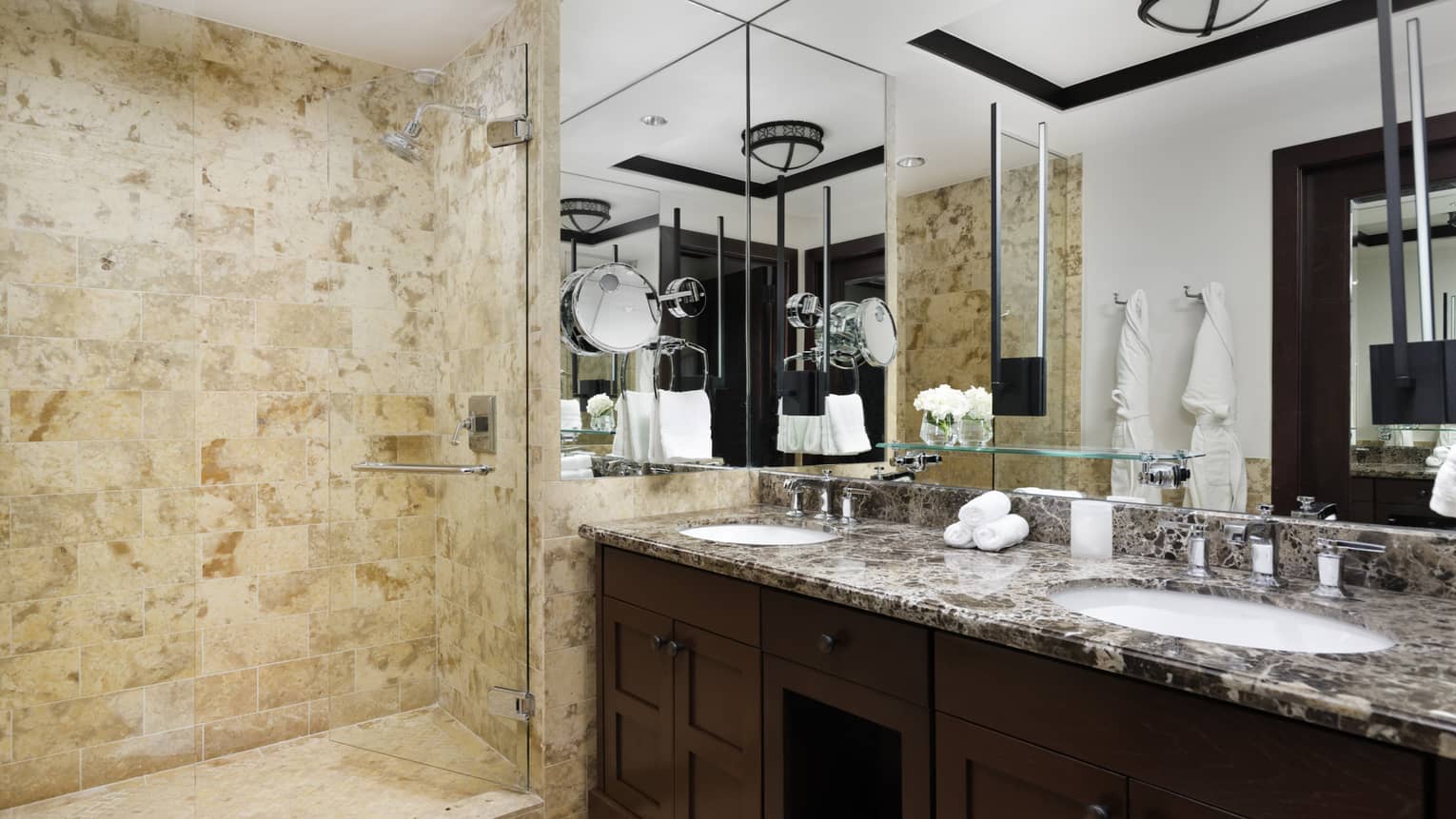 Bathroom with double vanity and tan, limestone walk-in shower