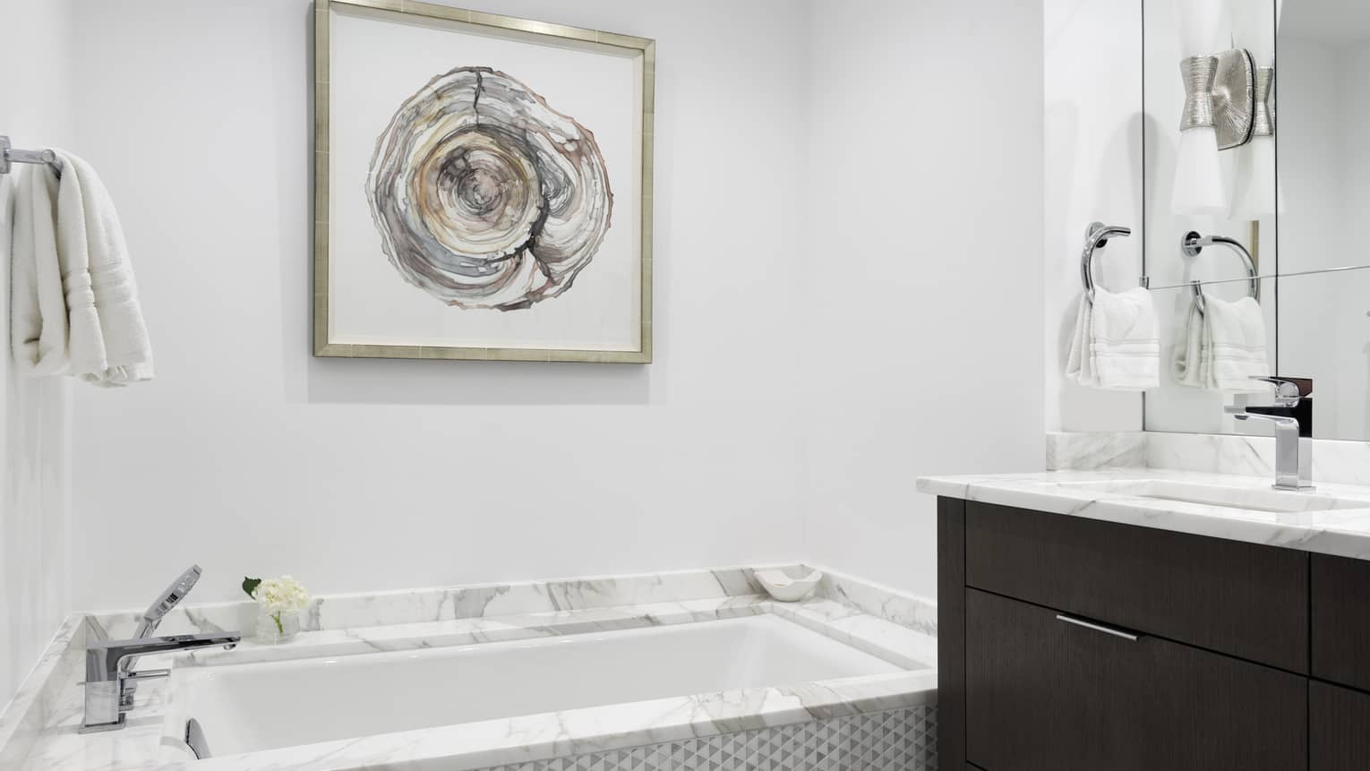 Bathroom with marble tub, artwork on wall, marble vanity